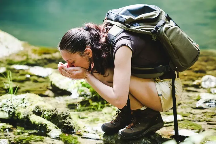 Girl with packpack drinking water from the spring